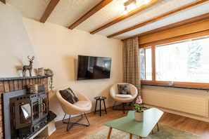 A cozy living room with a fireplace, two armchairs, a television, and a window with curtains. - A Luxurious Retreat Above Zermatt 1100 (Wallis)