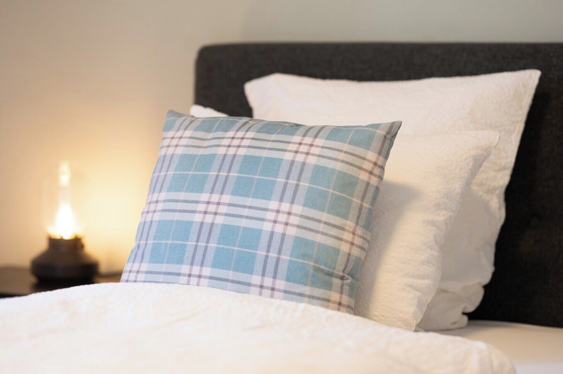 Een bed met twee kussens, waarvan één ruitpatroon heeft en één effen wit is.