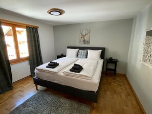 Ein Schlafzimmer mit einem Bett, zwei Nachttischen, einem Fenster mit Vorhängen, einem Bild an der Wand und einem Teppich auf dem Boden.