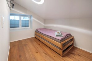 A small, single-bed room with a sloped ceiling, a window, and wooden flooring. - Elegant Escape in the Swiss Alps 1101 (Wallis)