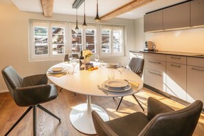 A dining area with a round table, chairs, and a view of the outside through large windows. - Elegant Escape in the Swiss Alps 1101 (Wallis)
