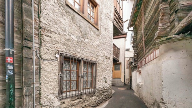 Une ruelle étroite bordée d’immeubles en pierre, avec une porte en bois et un portail en métal.