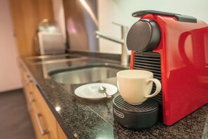 Una máquina de café roja con una taza sobre su base, un recipiente de vidrio y una tapa blanca sobre la encimera.