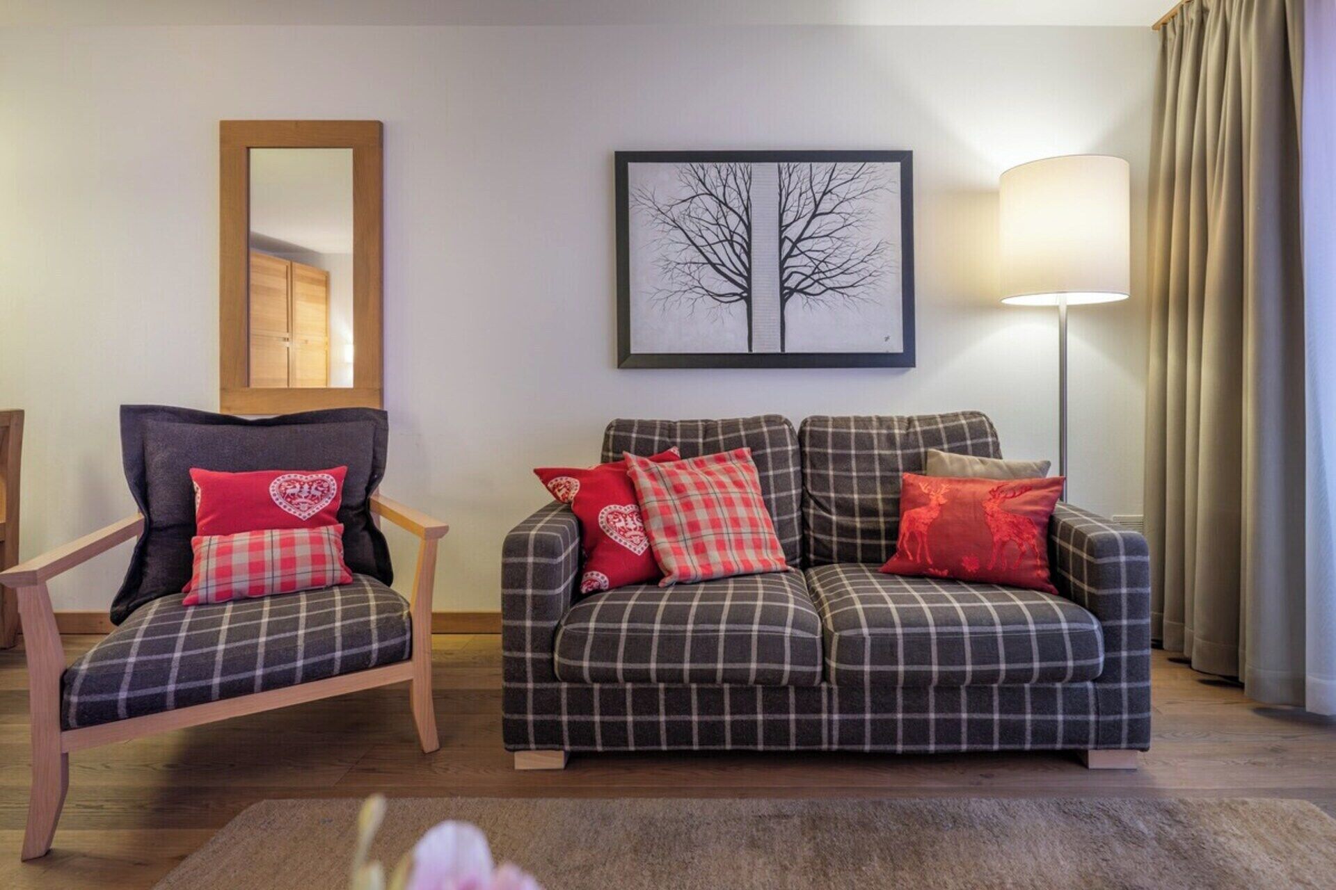 A living room with a sofa and armchair, a framed picture on the wall, and a floor lamp.