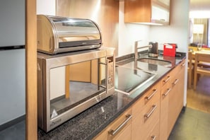 Eine kompakte Küche mit integriertem Mikrowellenherd und Toaster, Holzschränken und einer Arbeitsplatte aus Granit.