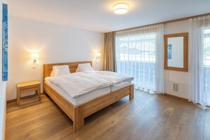 A hotel room with a wooden bed, bedside tables, and a large window with curtains. - Magic & Contemporary Alpine Comfort 1103 (Wallis)