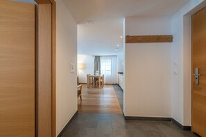 A hallway with a wooden door on the left, a coat rack on the right, and a dining area in the background. - Magic & Contemporary Alpine Comfort 1103 (Wallis)