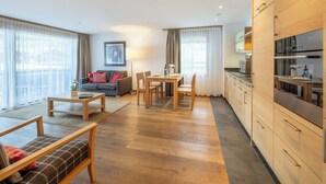 En moderne stue med sofa, spisebord og et køkken med træskabe og hårde hvidevarer.