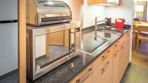 A compact kitchen with a built-in microwave and toaster, wooden cabinets, and a granite countertop. - A Serene Luxury Escape in the Swiss Alps 1104 (Wallis)