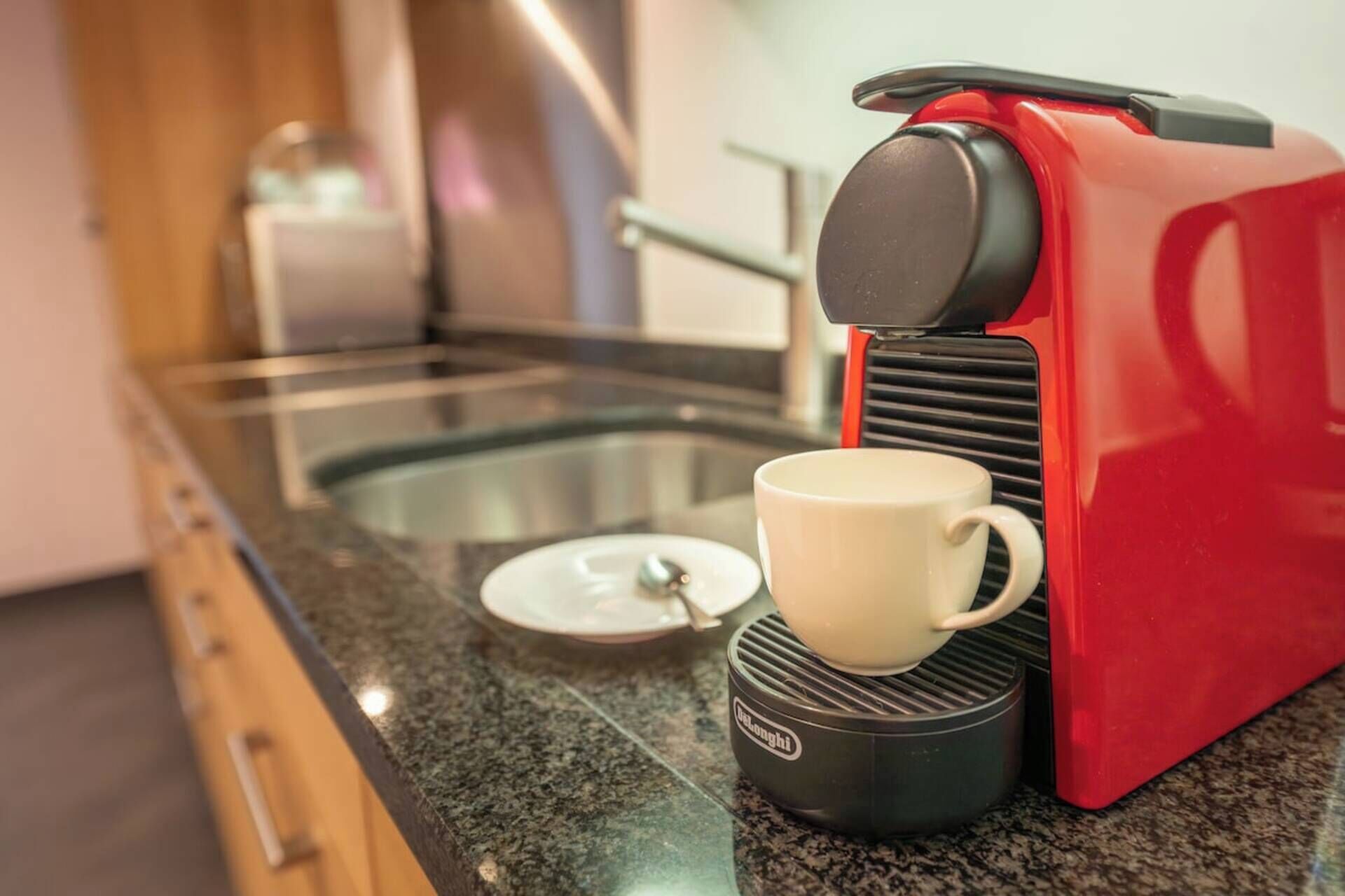 Eine rote Kaffeemaschine mit einer Tasse auf der Basis, einem Glasbehälter und einem Löffel auf der Arbeitsplatte.