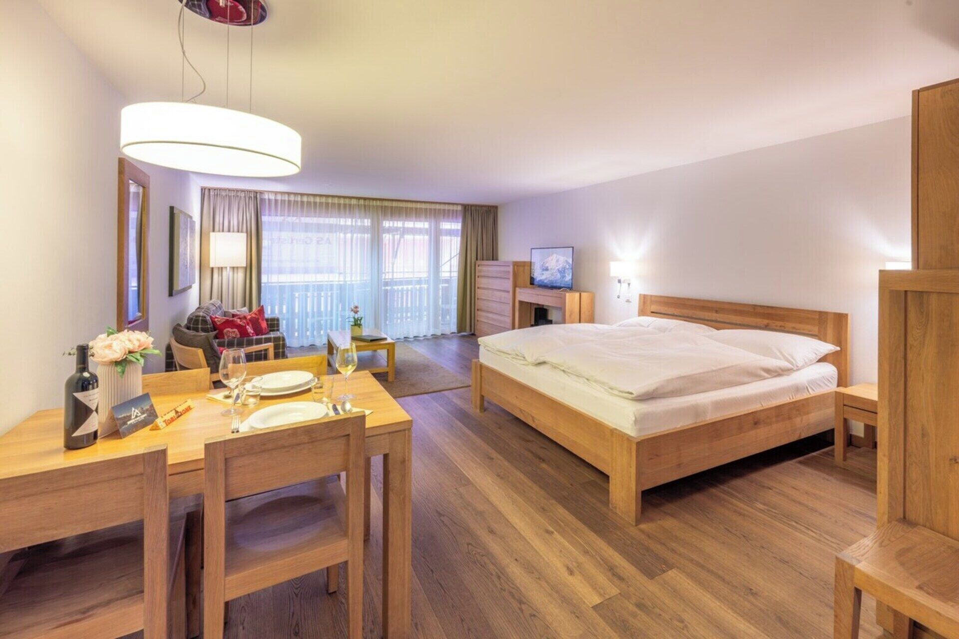A hotel room with a bed, a desk with a chair, a television, and a window with curtains.