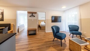 Ein modernes Hotelzimmer mit Holzboden, einem Bett, einem Schreibtisch, einem Stuhl, einem Fernseher und einem Fenster mit Vorhängen.