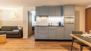 Eine moderne Küche mit grauen Schränken, einem eingebauten Backofen und einem Essbereich mit Tisch und Stühlen.