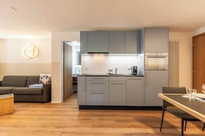Eine moderne Küche mit grauen Schränken, einem eingebauten Backofen und einem Essbereich mit Tisch und Stühlen.