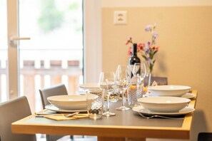 A dining table set with white plates, glasses, and cutlery, with a vase of flowers in the background. - Chic Alpine Retreat with Views 1095 (Wallis)