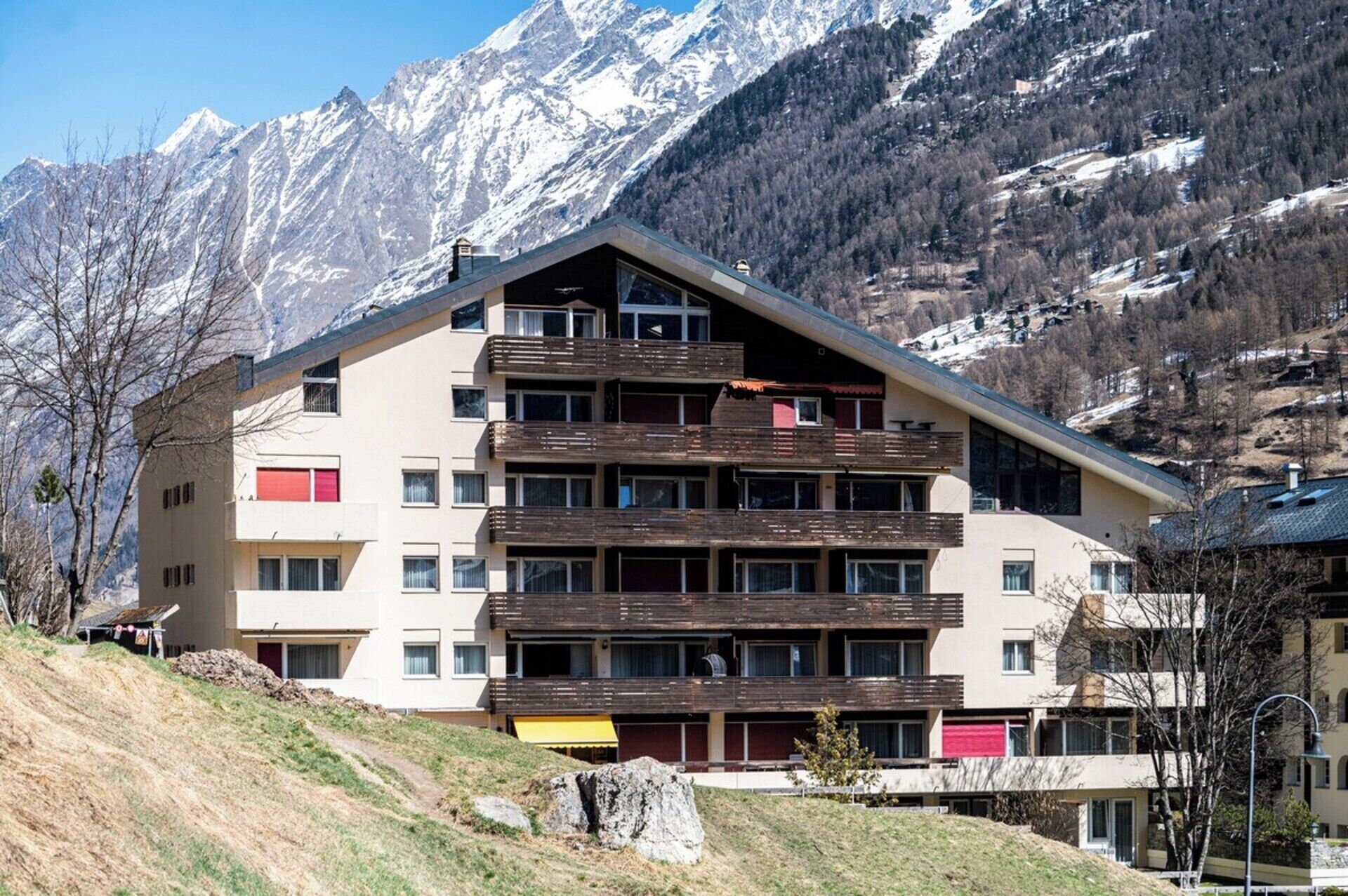 A multi-story hotel with balconies, set against a mountainous backdrop.