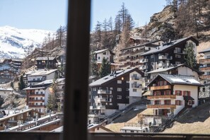 Ein Bergdorf mit mehrstöckigen Gebäuden, steilen Dächern und einer schneebedeckten Bergkette im Hintergrund.