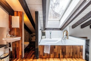 Un baño moderno con suelo de madera, una bañera blanca, un lavamanos y un tragaluz.