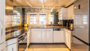 A modern kitchen with white cabinets, a black countertop, and a stainless steel refrigerator. - Alpine Serenity with Iconic Mountain Views 1090 (Wallis)