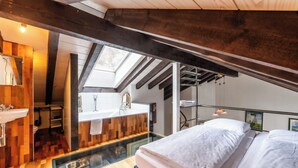 A bedroom with a skylight, a wooden floor, a bed, and a bathroom with a sink and mirror. - Alpine Serenity with Iconic Mountain Views 1090 (Wallis)