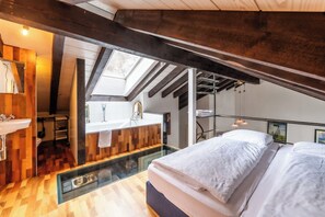 Ein Schlafzimmer mit Dachfenster, Holzboden, einem Bett und einem Badezimmer mit Waschbecken und Spiegel.