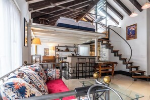 A modern loft with a high ceiling, exposed beams, a kitchen with bar stools, a red sofa, and a staircase. - Alpine Serenity with Iconic Mountain Views 1090 (Wallis)