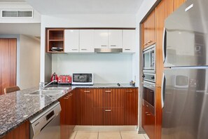 A modern kitchen with granite countertops, stainless steel appliances, and wooden cabinetry. - Ocean View 3BR Walk to Cavill Ave and the Beach (Surfers Paradise)