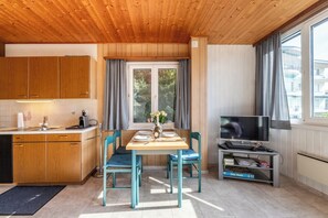 A compact kitchen with wooden cabinets, a dining table with chairs, a television, and a window with curtains. - Your Elegant  Mountain Retreat 1103 (Ticino)