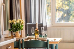 A dining table set with plates, a bottle of wine, and glasses, with a vase of flowers on the left. - Your Elegant  Mountain Retreat 1103 (Ticino)