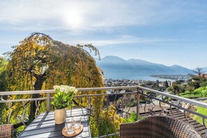 Ein Balkon mit Tisch, einer Blumenvase und Blick auf Stadt und Berge.