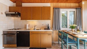 Uma cozinha compacta com armários de madeira, forno embutido e área de refeições com mesa e cadeiras.