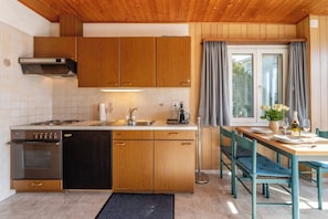 Eine kleine Küche mit Holzausbau, einem Einbauofen und einem Essbereich mit Tisch und Stühlen.