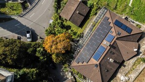 Um edifício residencial com telhado inclinado, painéis solares e uma entrada curva.
