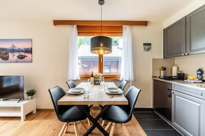 Ein Essbereich mit Holztisch, schwarzen Stühlen, einer Pendelleuchte und Blick auf einen Berg durch ein Fenster.