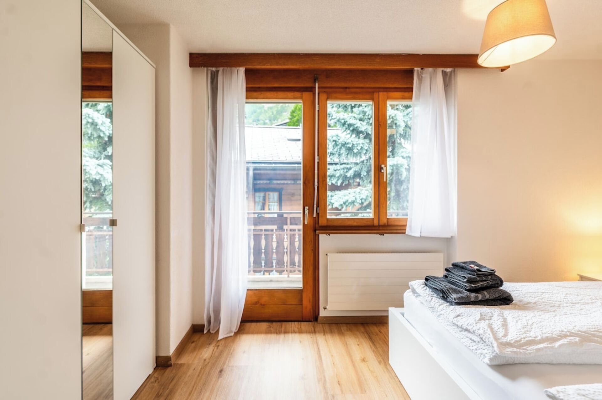 Ein Schlafzimmer mit Holzboden, einem Bett mit weißer Bettdecke, einem Heizkörper und einem Fenster mit Vorhängen.