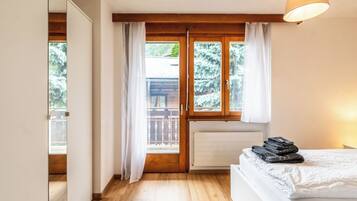Ein Schlafzimmer mit Holzboden, einem Bett mit weißer Bettdecke, einem Heizkörper und einem Fenster mit Vorhängen.