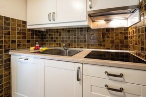 A kitchen with white cabinets, a stainless steel sink, and a tiled backsplash. - Effortless Alpine Living 1411 (Valais)