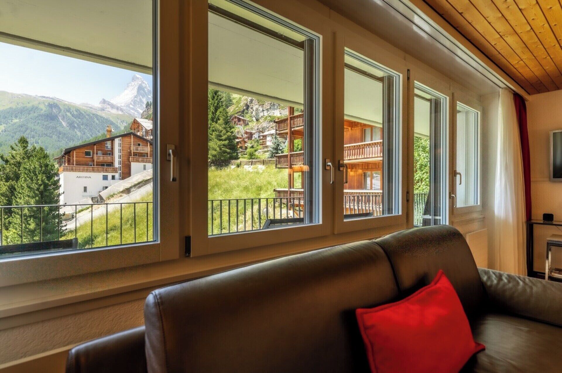 A room with a leather sofa, large windows with a view of a mountain and buildings, and a wooden ceiling.