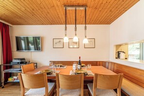 A dining area with a wooden table, four chairs, a television, and framed artwork on the wall. - Effortless Alpine Living 1411 (Valais)