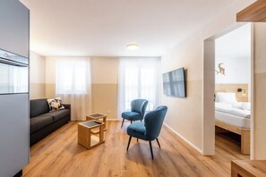Ein modernes Wohnzimmer mit einer Couch, zwei Sesseln, einem Couchtisch und einem an der Wand befestigten Fernseher.