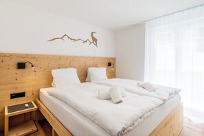 Ein Doppelbett mit weißer Bettwäsche, ein Holz-Kopfteil, zwei an der Wand befestigte Nachttische und ein dekoratives Wandbild.
