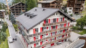 A multi-story hotel with balconies, a ski slope in the background, and a clear view of the surrounding area. - A Beautiful Alpine Escape in Zermatt 1092 (Wallis)