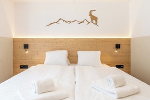 Ein Hotelzimmer mit einem hölzernen Kopfteil, zwei weißen Betten und einem Wandbild von einem Berg und einer Ziege.
