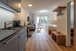 Een moderne keuken met een ingebouwde kookplaat, een eetgedeelte met een tafel en stoelen, een gezellig zithoekje met een bank, en een slaapkamer met een bed en een raam.