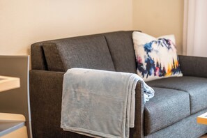 A grey sofa with a folded blanket and a colorful pillow. - Timeless Alpine Comfort,  Wallis 1093 (Wallis)
