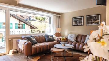Un salon avec un canapé en cuir marron, une table basse ronde et une vue sur un immeuble par le biais d’une grande fenêtre.