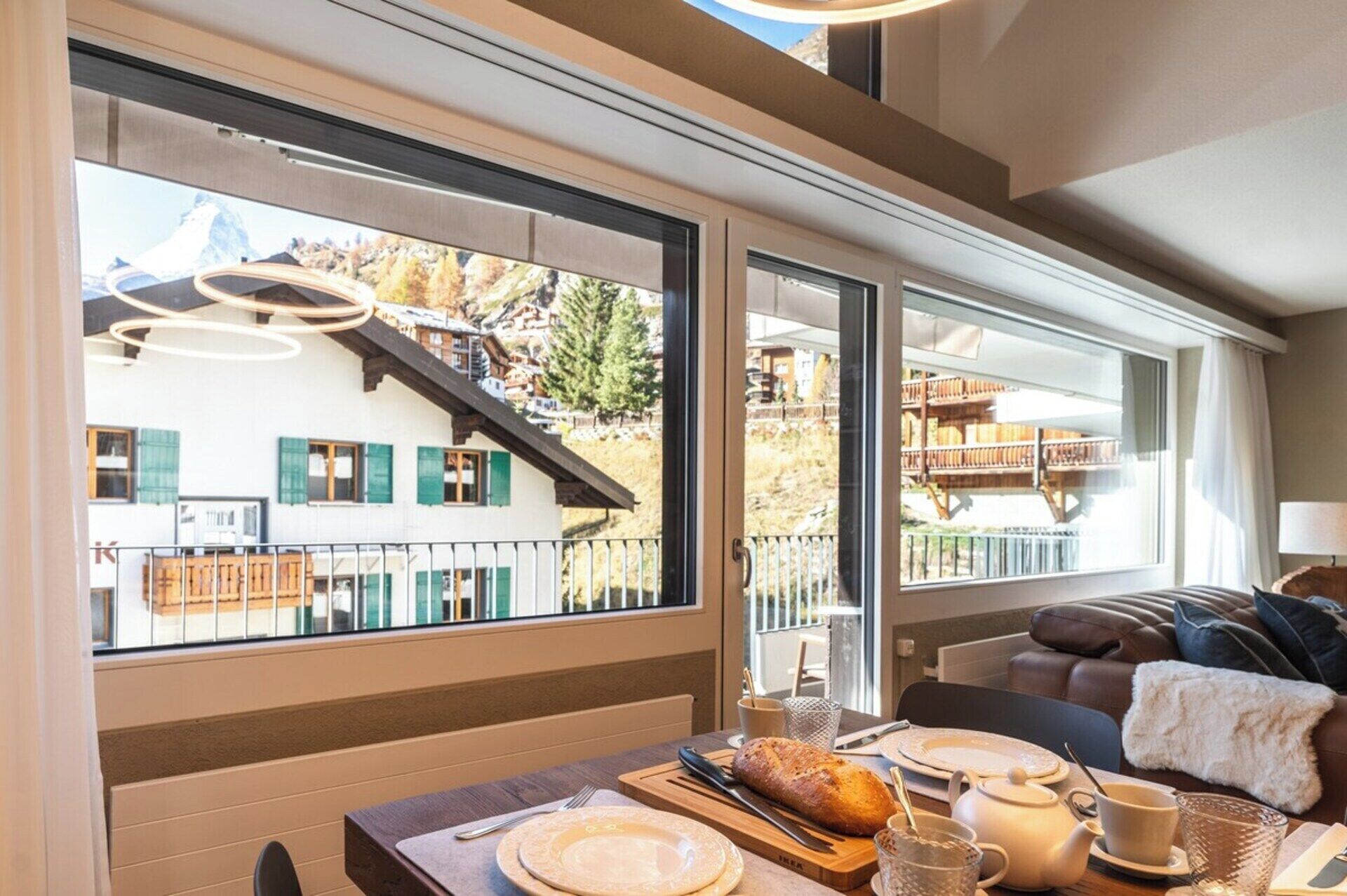 Un coin repas avec une table dressée pour deux personnes, un pain et une théière.