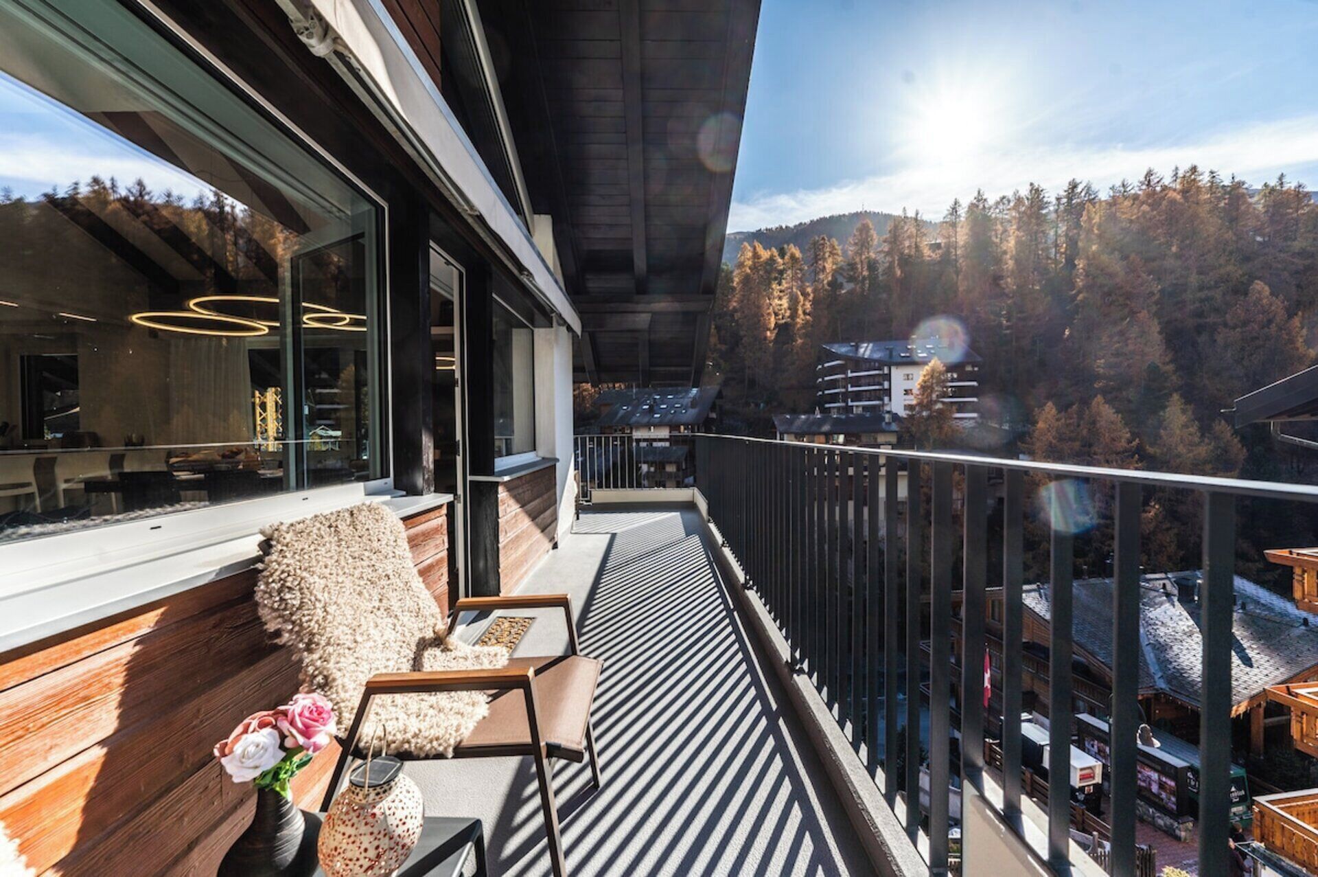 Un balcon offrant une vue sur une chaîne de montagnes boisée, un banc en bois et un coin repas aménagé avec un mobilier moderne.