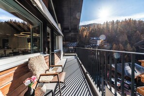 Un balcon offrant une vue sur une chaîne de montagnes boisée, un banc en bois et un coin repas aménagé avec un mobilier moderne.