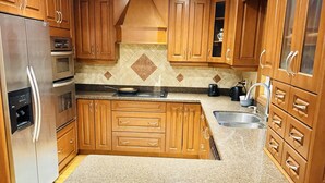 Eine Küche mit Holzausstattung, einem Edelstahlkühlschrank, einem Backofen und einer Arbeitsplatte aus Granit.